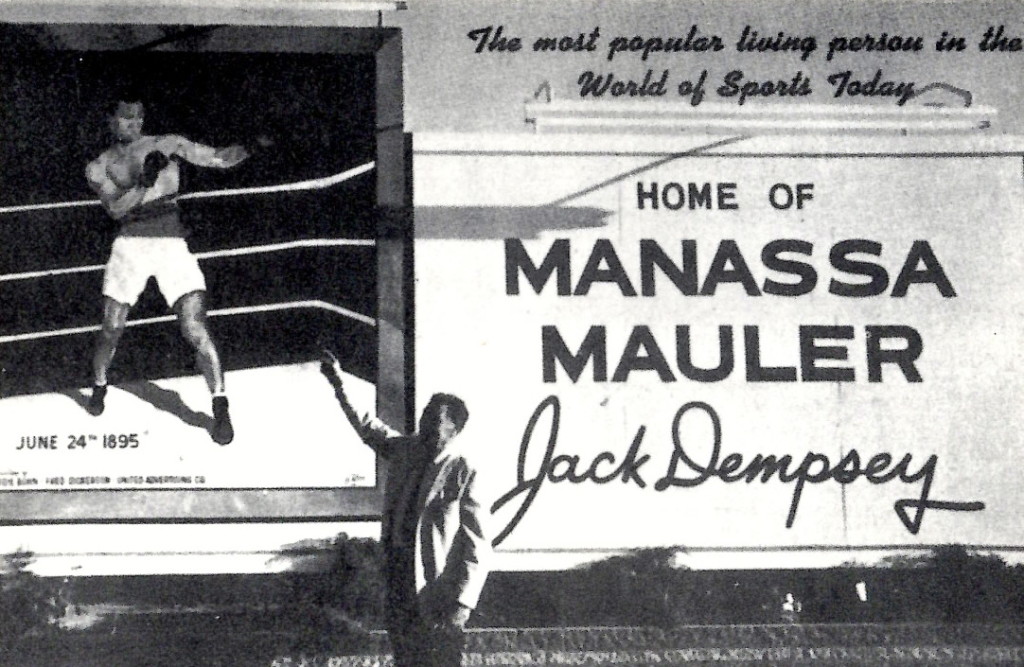 Jack Dempsey standing by sign in his hometown of Massassa, Colorado