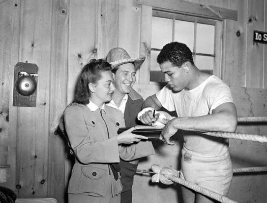 June 16 1941, Greenwood Lake, New York, USA --- Greenwood Lake, NY: Actress Olivia De Havilland who on numerous occasions has been hounded by autograph seekers, receives Joe Louis' autograph while actress Burgess Meredith looks on. They're pictured at Joe's Greenwood Lake, NY training camp where the world's heavyweight boxing champ is finishing up his chores before meeting Billy Conn of Pittsburgh in a championship bout at the Polo Ground, New York City on June 18th. --- Image by © Bettmann/CORBIS