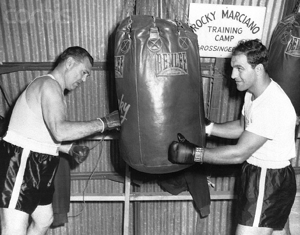 02 Sep 1954, Grossinger, New York State, USA --- Original caption: 9/2/1954-Grossinger, NY- Former heavyweight champion Jack Dempsey gets in a few licks for old times sake, as champ Rocky Marciano steadies the heavy bag for him at Rocky's training camp. Dempsey visited Marciano to watch him train for his forthcoming return bout with Ezzard Charles at Yankee Stadium September 15th. --- Image by © Bettmann/CORBIS
