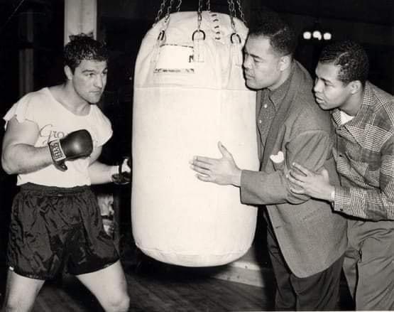 Heavyweight Champion Rocky Marciano in training with former Heavyweight Champion Joe Louis holding the bag.